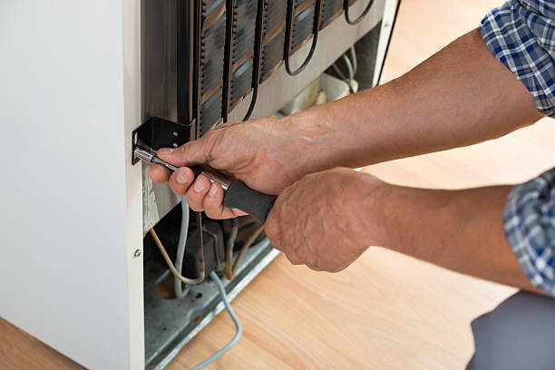Cropped image of serviceman working on fridge with screwdriver at home